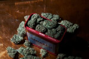 Dad Grass branded red tin overflowing with cannabis flower buds scattered on a wooden surface