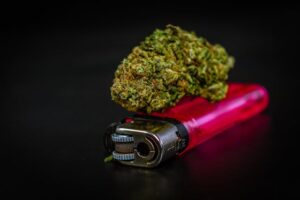 Cannabis bud resting on a pink lighter against a dark background, Delta-9 THC flower close-up